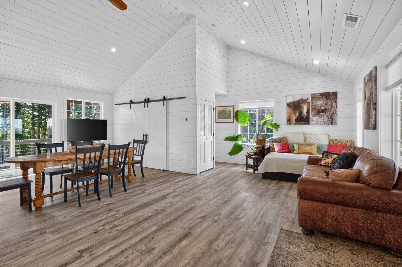A spacious living area with a dining table, a brown leather sofa, and a large window providing natural light.