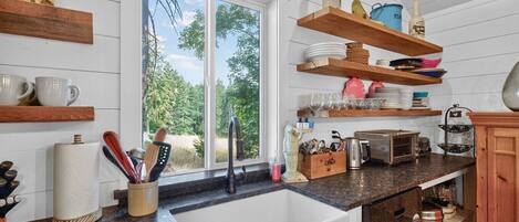 Eine Küche mit einem großen Fenster, Holzregalen und verschiedenen Küchenutensilien.
