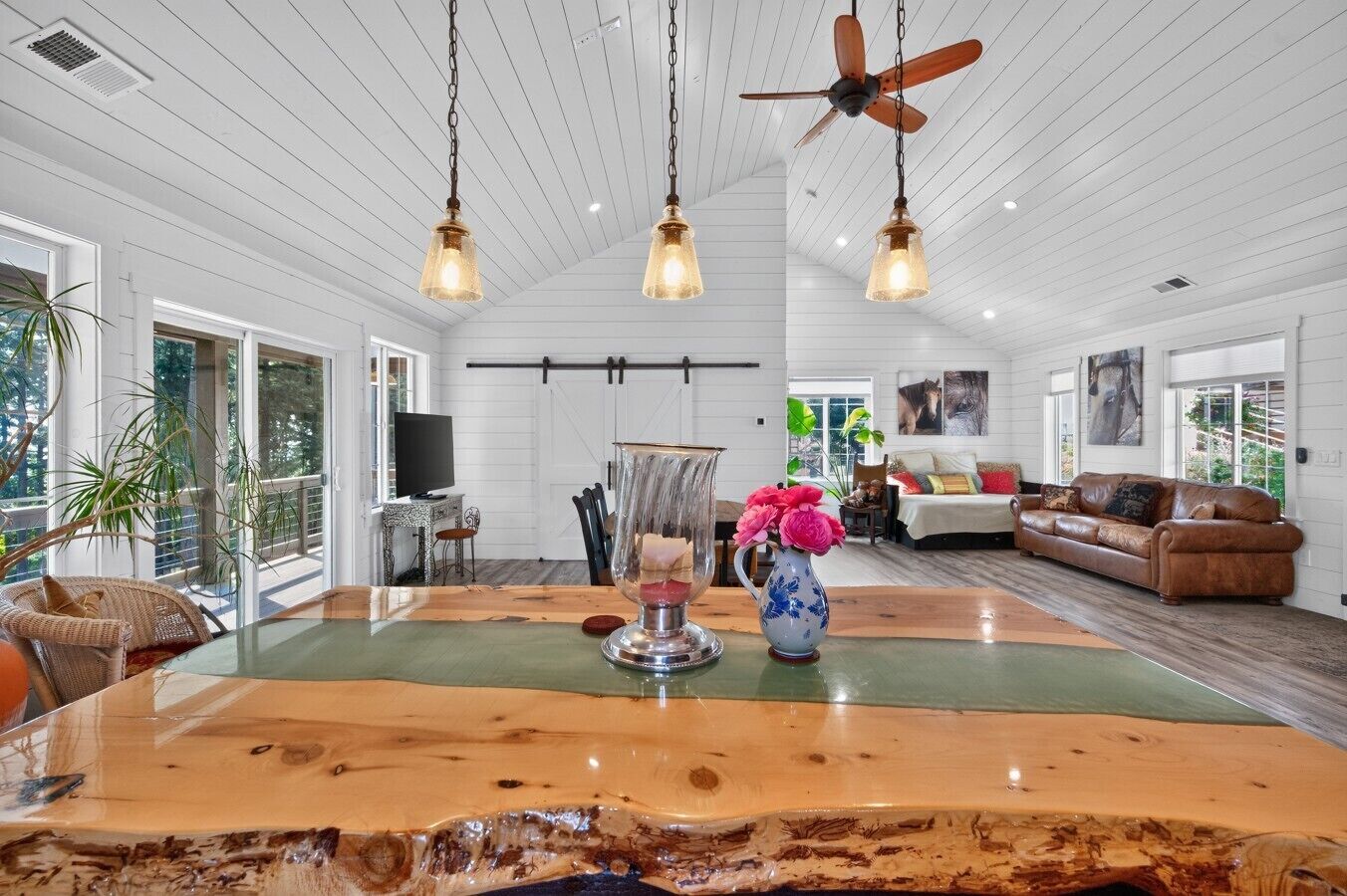 A spacious room with a large wooden dining table, a ceiling fan, and a view of the outdoors.