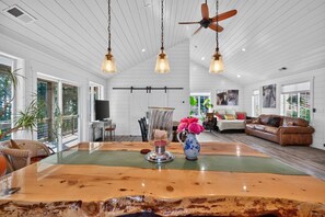 A spacious room with a large wooden dining table, a ceiling fan, and a view of the outdoors.