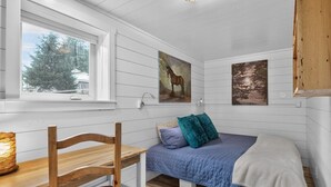 Une chambre à coucher avec un lit, une chaise, une fenêtre et des œuvres d’art accrochées aux murs.