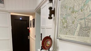A hallway with a wooden floor, a white wall with a map, and a brick fireplace with decorative items. - Hotel Entree - Private Balcony View of Canal (Brugge)