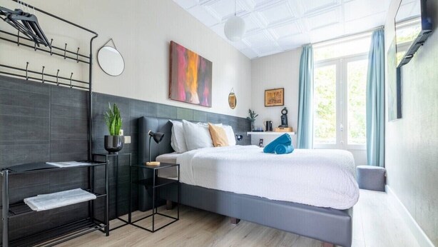 A modern bedroom with a bed, bedside tables, a hanging coat rack, and a window with curtains. - Hotel Entree - Private Balcony View of Canal (Brugge)