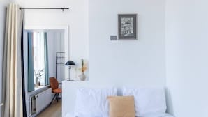 Un dormitorio con una cama, una silla, una lámpara, un cuadro enmarcado y vistas de una cocina y comedor.
