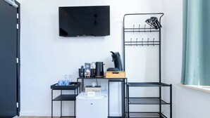 Habitación de hotel compacta con televisión de pantalla plana, un refrigerador pequeño, una cafetera, una caja de pañuelos y un perchero de metal con ganchos.