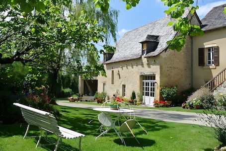 A stone building with a sloped roof, a front door, and a small porch with potted plants.. Guest Room “La Grange De La Bonaurie - Sienne” with Shared Terrace, Garden, and Wi-Fi