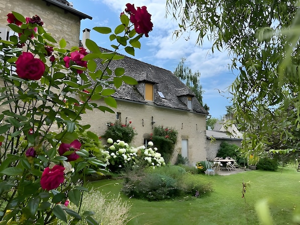 A rustic building with a stone facade, a sloped roof, and a garden with roses and greenery.
