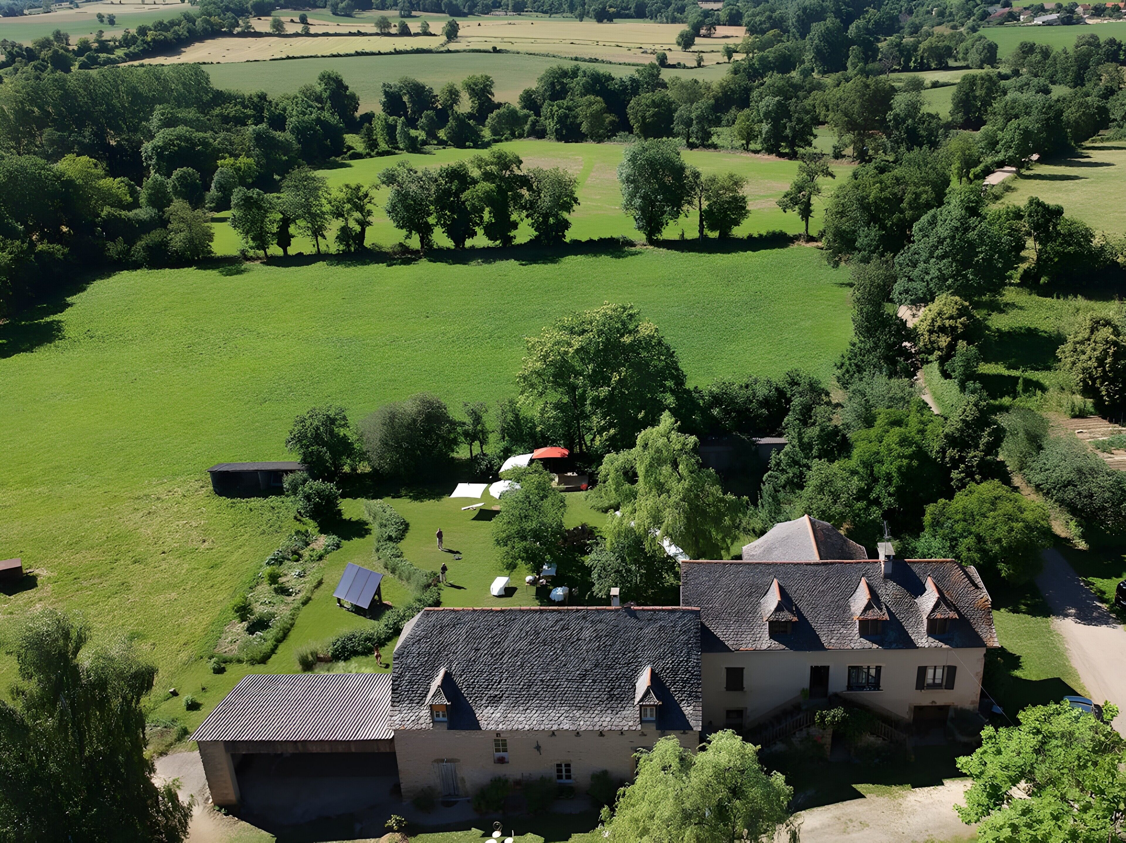 A large estate with expansive green fields, a central building with a steep roof, and surrounding trees.