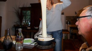 A person using a cheese slicer in a kitchen with a dining table, chairs, and various kitchen appliances. - Guest Room 'La Grange De La Bonaurie - Havane' with Shared Terrace and Garden (Anglars-Saint-Félix)