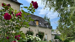 A traditional stone building with a sloped roof, surrounded by lush greenery and flowering plants. - Guest Room 'La Grange De La Bonaurie - Havane' with Shared Terrace and Garden (Anglars-Saint-Félix)