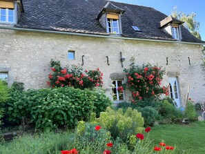 A stone building with multiple windows, a sloped roof, and a garden with red flowers.