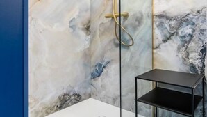 Ett modernt badrum med en vägg av marmor, ett guldfärgat duschmunstycke och en svart hylla.