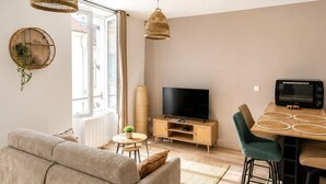 Een moderne woonkamer met een bank, televisie, eettafel en rieten hanglampen.