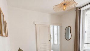 Een slaapkamer met een bed, een deur, een raam en een hangende lamp.