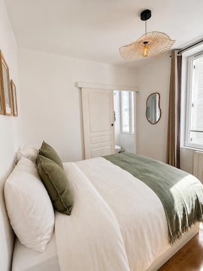 Une chambre à coucher avec un lit, une porte, une fenêtre et un luminaire suspendu.