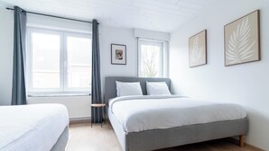 Ein Schlafzimmer mit einem Bett, einem Nachttisch, einem Fenster und zwei gerahmten Blätterbildern an der Wand.