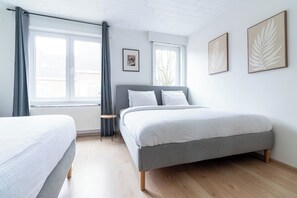 A bedroom with a bed, a bedside table, a window with curtains, and two wall-mounted leaf-patterned artworks.