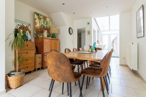 A dining area with a wooden table, brown chairs, a cabinet, a plant, and a window.