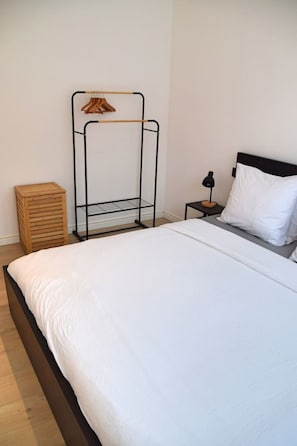 A bedroom with a bed, a wooden bedside table, a black nightstand, a black lamp, a white pillow, and a wooden wardrobe.