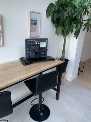 A workspace with a wooden desk, a black chair, a potted plant, and a framed picture on the wall.