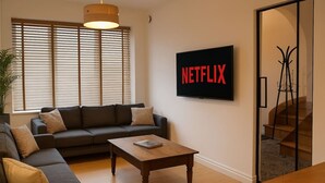 Un salon avec un canapé, une table basse et un téléviseur fixé au mur qui affiche le logo « NETFLIX ».