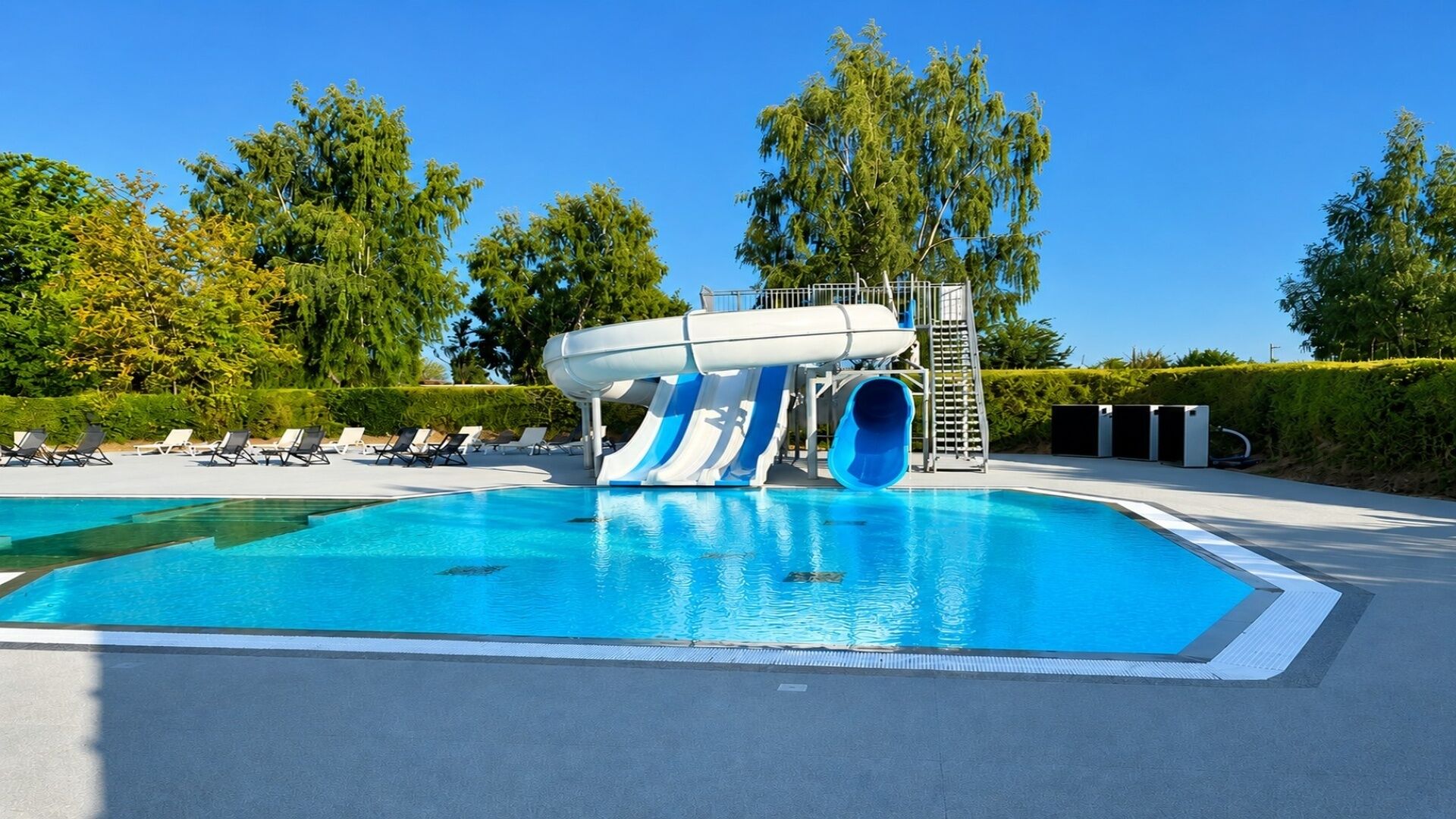 A swimming pool with a water slide and lounge chairs.