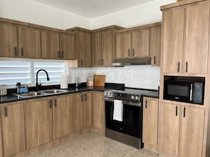 Una cocina con armarios de madera, un lavamanos de acero inoxidable, un microondas negro y un horno de acero inoxidable.