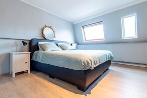 Ein Schlafzimmer mit einem Bett, Nachttischen, einem Spiegel und zwei Fenstern.