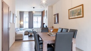 A modern living room with a sofa, dining table, and chairs, a kitchen area, and a large window with curtains. - Spacious Bruges House with Free Parking (Brugge)