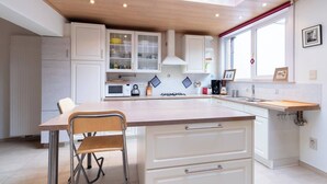 A modern kitchen with white cabinets, a wooden dining table, and a window with a red curtain. - Spacious Bruges House with Free Parking (Brugge)