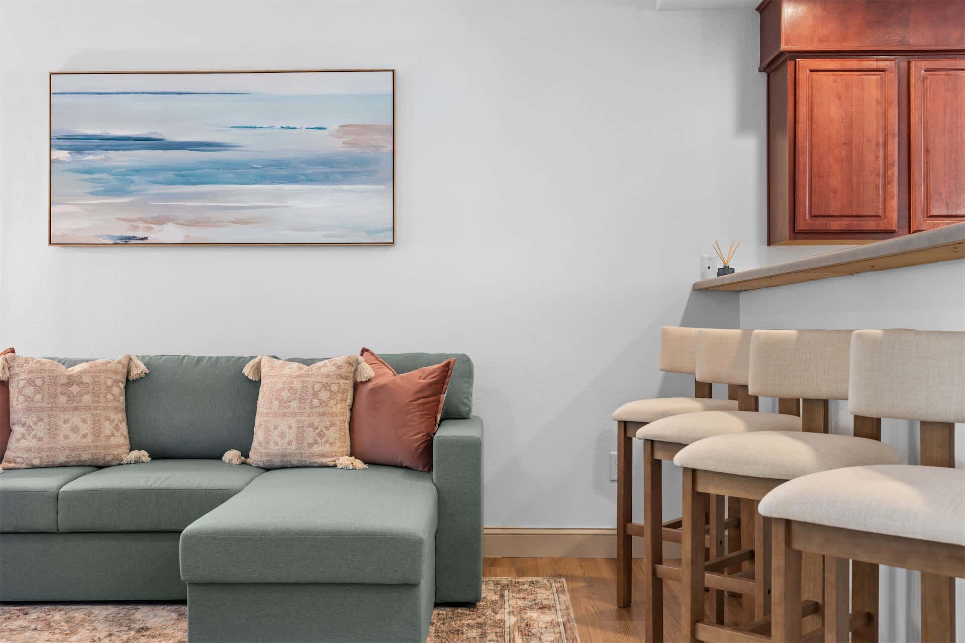 A living room with a green sofa, patterned cushions, a wooden coffee table, and a view of the kitchen.