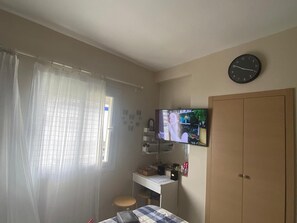 A room with a bed, a desk, a television, a wardrobe, and a window with curtains. - Elegant Apartment in a Secured Residence with Pool Near the Beach (Bouznika)