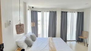 A bedroom with a bed, a bedside table, a chair, and a hanging light fixture.