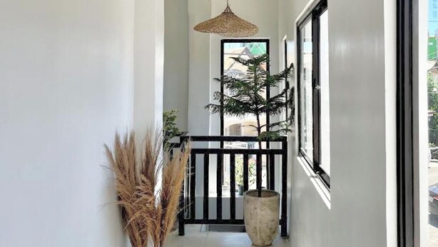 A corridor with a white wall, a large window, a hanging woven light fixture, and a potted plant.