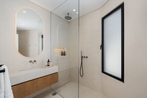 Een moderne badkamer met een douchecabine van glas, een grote spiegel en een wastafelmeubel met een houten kastje.