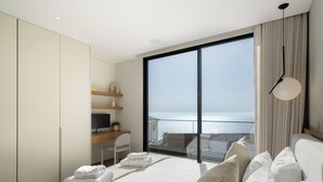 A modern hotel room with a large bed, a desk with a computer, a chair, and a view of the sea through a large window. - Superb modern villa with pool in Calheta|Amani (Arco Da Calheta)