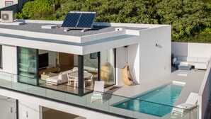 A modern house with a glass-enclosed swimming pool, solar panels, and a white exterior. - Superb modern villa with pool in Calheta|Amani (Arco Da Calheta)