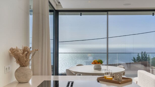 A modern room with a large window, a round table with a fruit bowl, a laptop, and a tray with a glass of orange juice. - Superb modern villa with pool in Calheta|Amani (Arco Da Calheta)