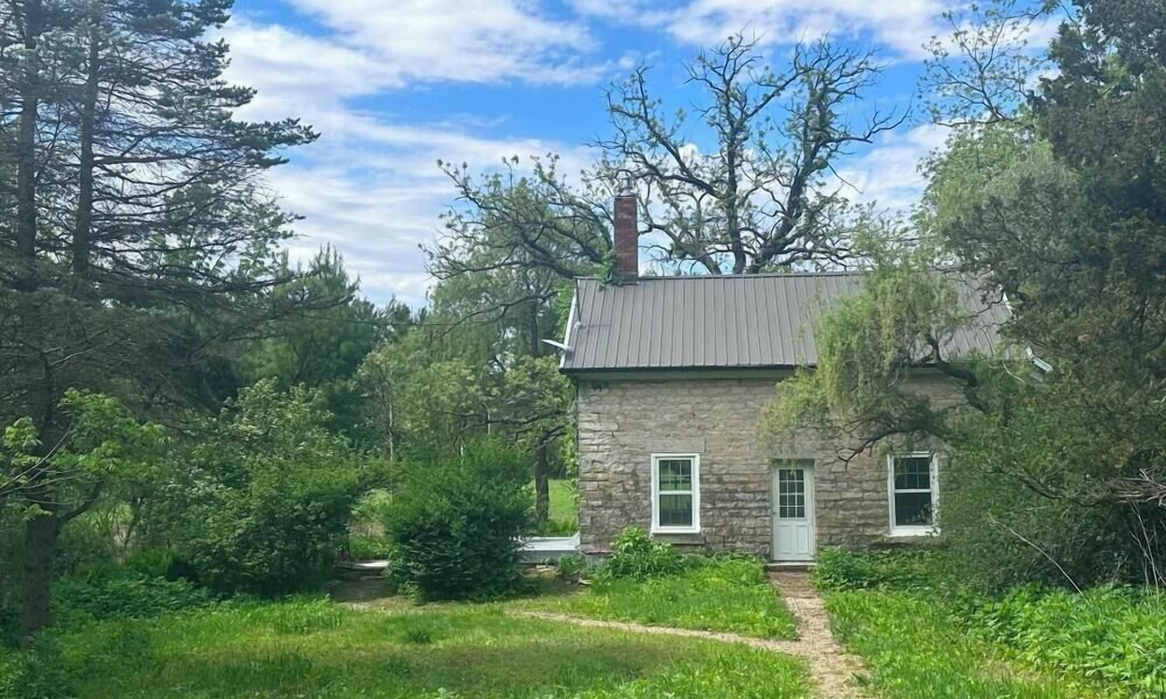 A stone house with a metal roof, surrounded by dense greenery and trees.