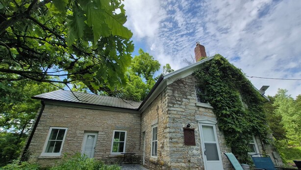 A stone house with a sloped roof, a chimney, and a small porch area with outdoor seating. - Secluded 1860 Stone House recently remodeled on the Upper Iowa River by Bluffton (Decorah)