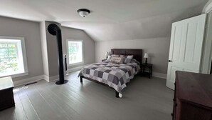 A bedroom with a bed, a nightstand, a dresser, a ceiling fan, and a door. - Secluded 1860 Stone House recently remodeled on the Upper Iowa River by Bluffton (Decorah)