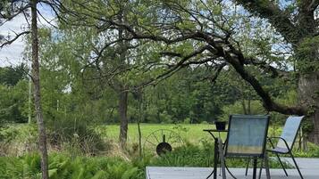 Un terrazzo in legno con due sedie e un tavolo, immerso nel verde e alberi.