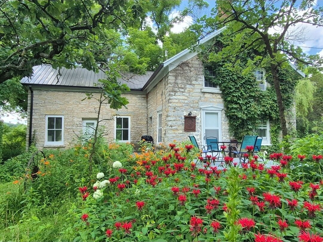 Une maison en pierre avec un jardin devant, une terrasse avec des chaises et une petite table.
