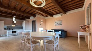 A dining area with a round table and chairs, a kitchen in the background, and a ceiling with exposed wooden beams. - Spacious Holiday Home With Shared Pool in Poppi (Poppi)