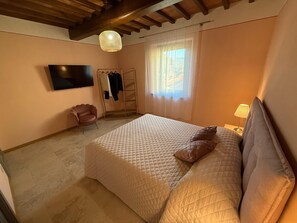 A bedroom with a bed, a TV, a chair, a clothes rack, and a window. - Spacious Holiday Home With Shared Pool in Poppi (Poppi)