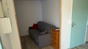 Een kamer met een grijze bank, een houten dressoir en een blauwgroene deur.
