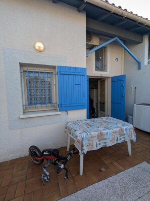 A house with a blue door, a window with a metal grill, and a table with a patterned tablecloth.