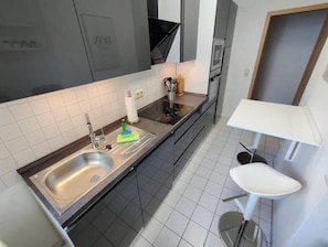 Eine moderne Küche mit Spüle aus Edelstahl, einer weißen Arbeitsplatte und einem kleinen Tisch mit einem Stuhl.