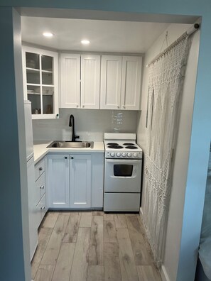 A compact kitchen with white cabinets, a stainless steel sink, a stove, and a patterned curtain.