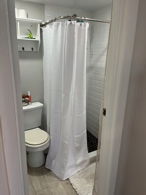 Un baño con inodoro blanco, cortina de ducha y una alfombra blanca.